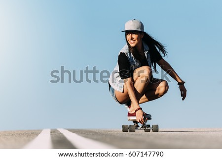 Beautiful young skater woman riding on her longboard in the city. Royalty-Free Stock Photo #607147790