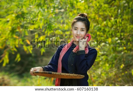 Beautiful girl in Laos wear traditional dress smile and carry the large basket or rice winnowing basket on green and vintage background