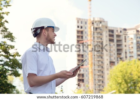 Engineer builder stands with a digital tablet on the background of the house under construction.