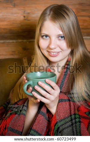 The beautiful girl with a long blond hair drinks tea having wrapped in a plaid