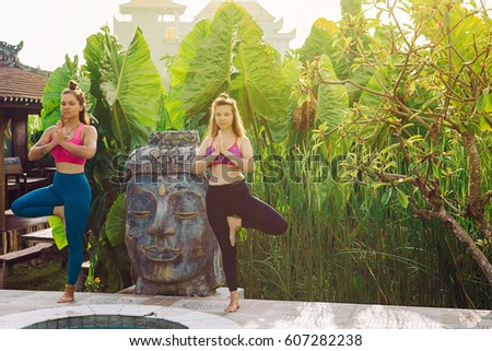 Young women practicing yoga during luxury yoga retreat in Asia, Bali, meditation, relaxation, getting fit, enlightening, green grass jungle background. Tree pose