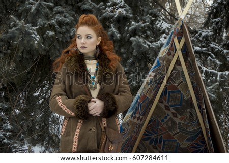  Beautiful young nordic rad haired girl in north ethnic clothes standing in the winter forest landscape near the wigwam