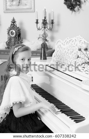 Beautiful, elegant little girl holding hands on the keys of a white Grand piano. Girl playing at the Christmas concert in the music school.