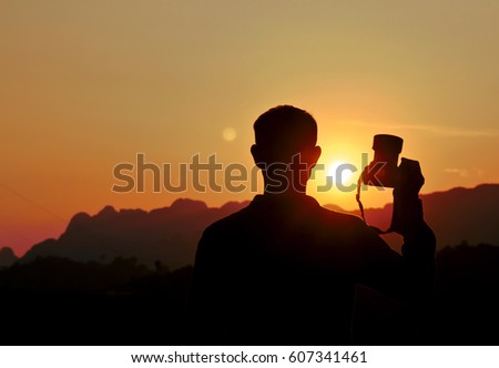 Photographer silhouette handing camera at sunset background.