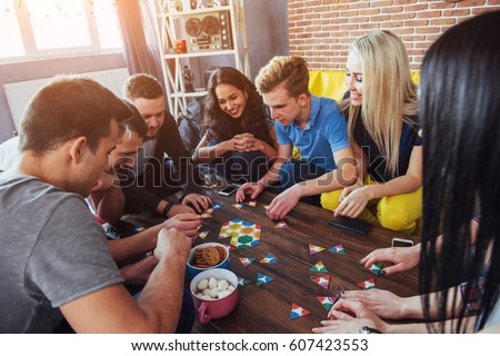 Group of creative friends sitting at wooden table. People having fun while playing board game. Royalty-Free Stock Photo #607423553