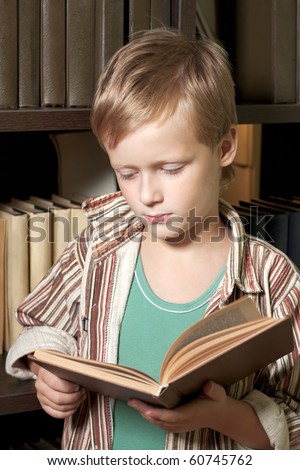 The boy reads the book with a serious face. The sight is directed on the book.