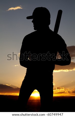 A man standing in the sunset holding his bat.