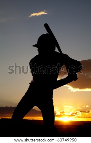 A man standing in the sunset holding his bat ready to swing
