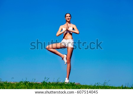 Young slim woman exercising in the park on a background of blue sky