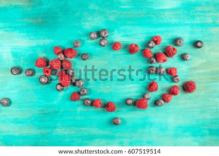 Fresh blueberries and raspberries, forming a frame on a vibrant turquoise background with a place for text
