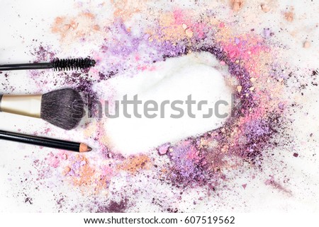 Makeup brush, pencil, and mascara applicator on white marble background, with traces of powder forming a frame. Horizontal template for a makeup artist's business card or flyer design, with copy space