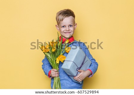Handsome boy holding flower bunch and gift box. Valentine's day. Birthday. Mother's day. Studio portrait over yellow background