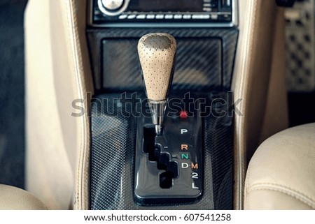 Automatic gear shift handle on carbon fiber panel in modern car.