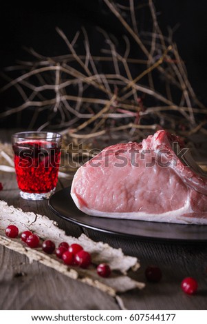 Still life of fresh game meat on a wooden table, surrounded by branches, herbs and wild berries