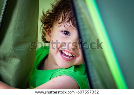 Portrait of cute little baby boy having fun outside hiding in a tent. Smiling happy child playing outdoors camping Royalty-Free Stock Photo #607557032