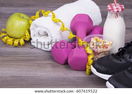 Fitness concept with a bottle of yogurt, apple, weights,towel and sneakers on a wooden background. With empty space for your text