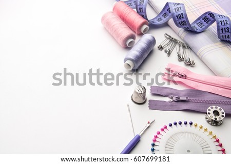 Sewing supplies and accessories for needlework. Fabric, spools of thread, scissors and thimbles on white background. Royalty-Free Stock Photo #607699181