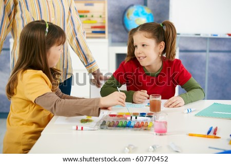 Elementary age children sitting around desk enjoying painting with colors in art class at primary school classroom.?