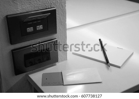 Electric switch, key card, Note book and pencil in the room, black and white.