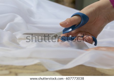 The woman cuts the fabric with scissors for sewing curtains on the window. The fabric lies on the floor. Side view.
