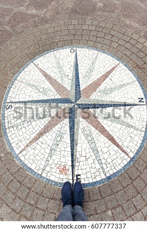 Looking at mosaic compass rose background and woman modern stylish sneakers on the stone brick floor from above. Alsace region, France. Colored outdoors vertical image with slightly vintage effect.