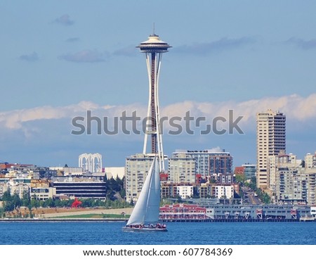 Beautiful summer day on Elliott Bay in Seattle, Washington with a sailboat on the water floating by a couple of Seattle's landmarks from the 1962 World's Fair: Seattle Center arches and Space Needle. Royalty-Free Stock Photo #607784369