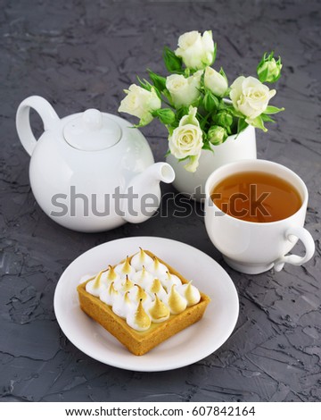 Lemon meringue pie, cup of tea, white roses and  teapot gray cement table. Selective focus, vertical image.