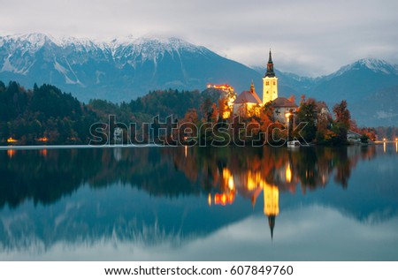Amazing night view on famous illuminated pilgrimage church of the Assumption of Blessed Mary and island on Bled Lake, Slovenia with reflection in water and the Alps on background.