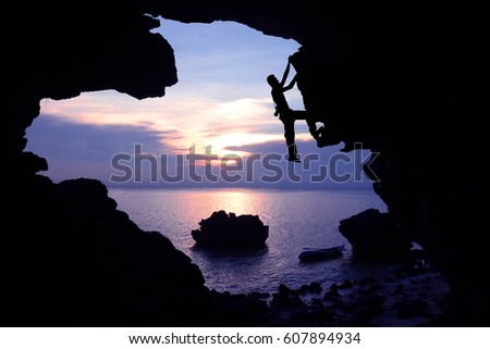 Photographer climbing rock in the cave near the beach with kayaking and purple sky sunset.