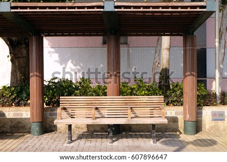 Public outdoor wood chair on footpath with a roof with sunshine
