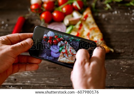 man using smartphone to take picture of slice of pizza on wooden table
