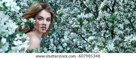 A beautiful young girl stands among the flowering trees. White flowers. Spring. A girl with her hair in a white dress. Portrait. Romance. Royalty-Free Stock Photo #607985348
