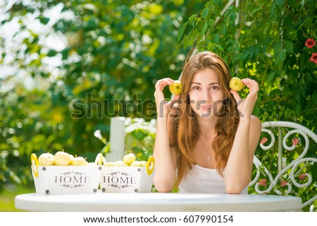 Girl with apples. Beautiful young girl with red hair is having fun. The girl is sitting at the table and holding the green apples. Baskets with fruit on the table. Vitamins spring 
