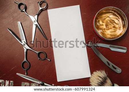 Blank card with barber tools flat lay. Top view on red table with scissors, razor, hair wax and shaving brush with empty white paper, free space. Barbershop, manhood concept