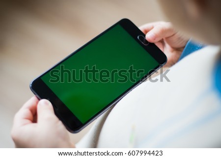 The child is holding a phone in his hand with a green screen for chroma keyer