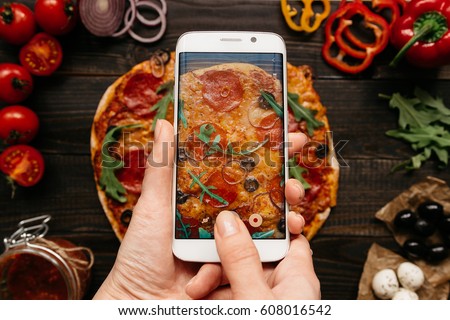 Photographing food. Hands taking picture of delicious pizza with smartphone.