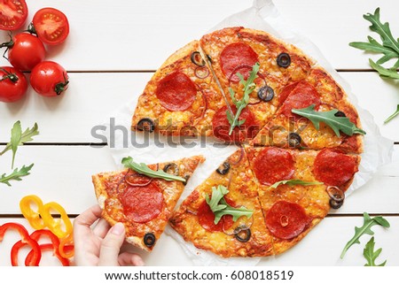 Eating pizza, top view. Hand taking slice of hot delicious pizza on the white wooden table.