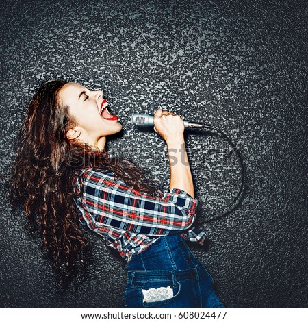 Karaoke party. Time to sing! Crazy casual curly chic girl singing with microphone. Studio shot Royalty-Free Stock Photo #608024477