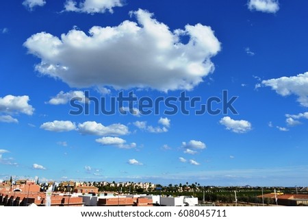 A bright sunny day in autumn in Spain. White fluffy clouds float above houses and orange gardens . The clouds are so low, it seems that you can touch them with your hand .