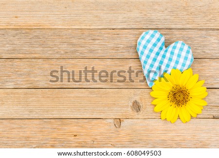 Bavarian background with blue-white checkered fabric heart and sunflower on rustic wood  for Oktoberfest.