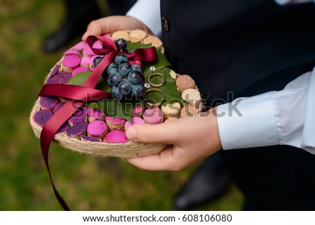 Golden wedding rings, grapes and champagne corks wedding decor, close-up. Rustic wedding ring bearer pillow. Royalty-Free Stock Photo #608106080
