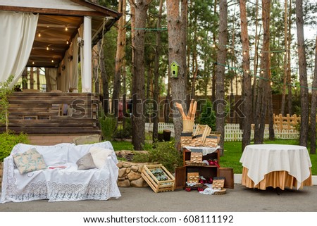 Rustic wedding decor, summer pavilion, string lights and couch with handmade pillows. Forest trees on the background. Photo zone.