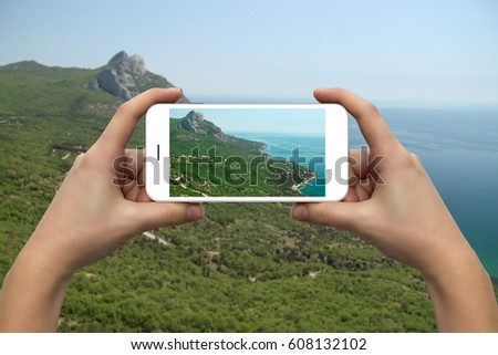 Female hands with a smartphone close-up. Photographing the coast of the sea and mountains.
