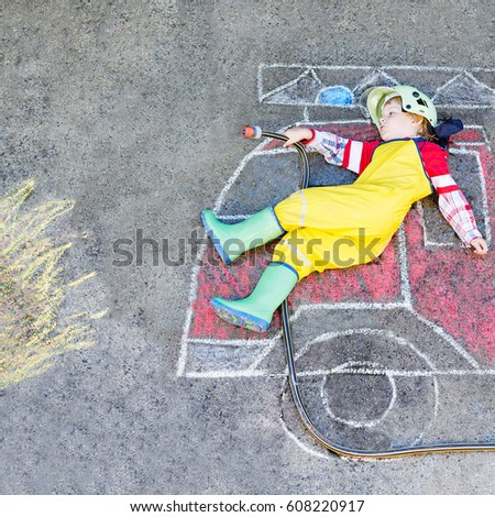 Creative leisure for kids: adorable toddler child  having fun with fire truck picture drawing with chalk, outdoors. Dreaming of future profession.