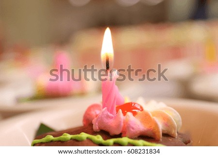 closeup of some unlit candles and just one lit candle after blowing out the cake.