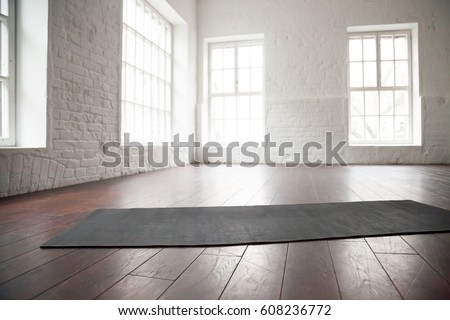 Empty white space in fitness center, white brick walls, natural wooden floor and big windows, modern loft studio, unrolled yoga mat on the floor, comfortable open area for sport and exercises Royalty-Free Stock Photo #608236772