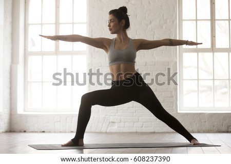 Young yogi woman practicing yoga, standing in Warrior two exercise, Virabhadrasana II pose, working out wearing sportswear bra and pants, full length, white loft studio background. Weight loss concept Royalty-Free Stock Photo #608237390