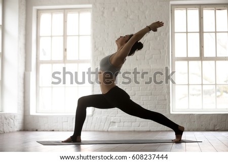 Young attractive woman practicing yoga, standing in Warrior one exercise, Virabhadrasana I pose, working out, wearing sportswear, full length, white studio background, side view. Weight loss concept Royalty-Free Stock Photo #608237444