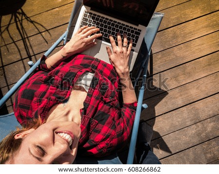 Young woman enjoying the sun, sitting on a patio with her laptop