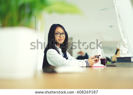 Portrait of smiling chinese student chatting with friends on smartphone using 4G free internet connection.Happy beautiful young asian hipster girl in glasses studying in library and looking on camera